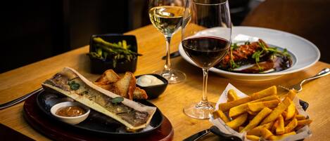 A dining table with a plate of food, two glasses of wine, a knife, and a basket of fries.