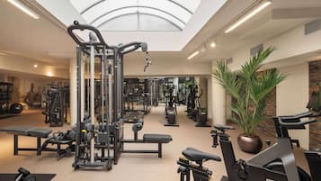 Un gimnasio con diferentes máquinas de ejercicio, un tragaluz y una planta en maceta.