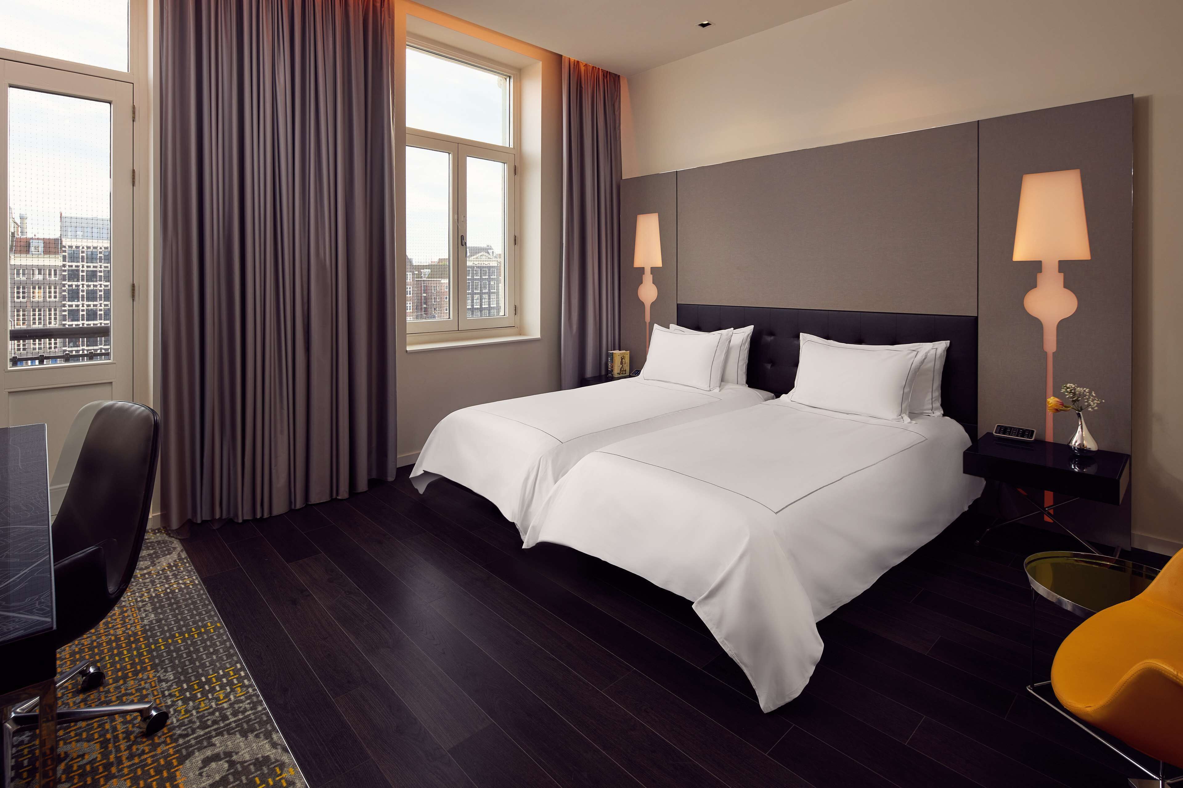 Hotelkamer met een groot bed, een bureau, een stoel, een lamp en uitzicht op de stad door een raam.