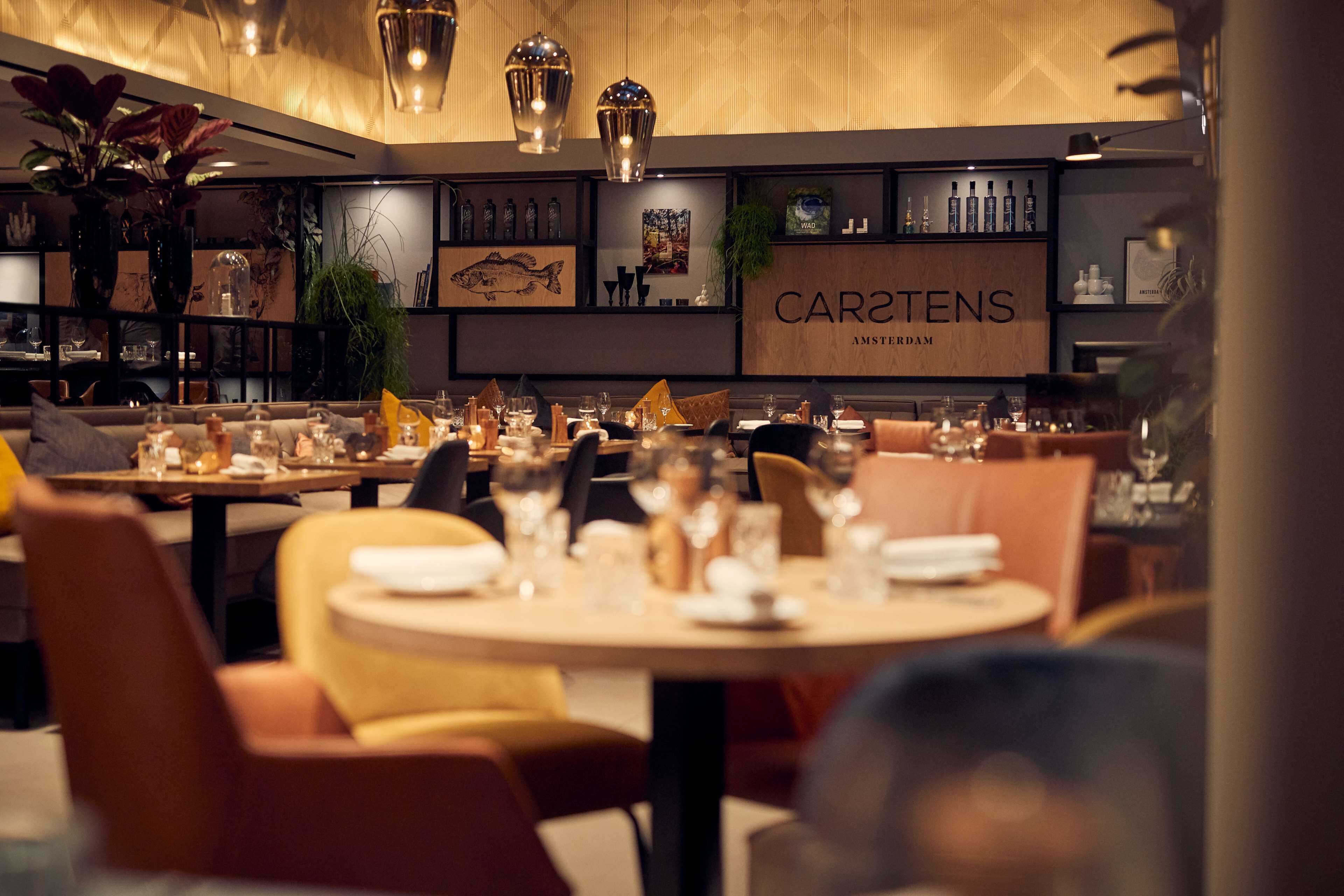 A restaurant interior with round tables, chairs, and a variety of dishes and glasses.