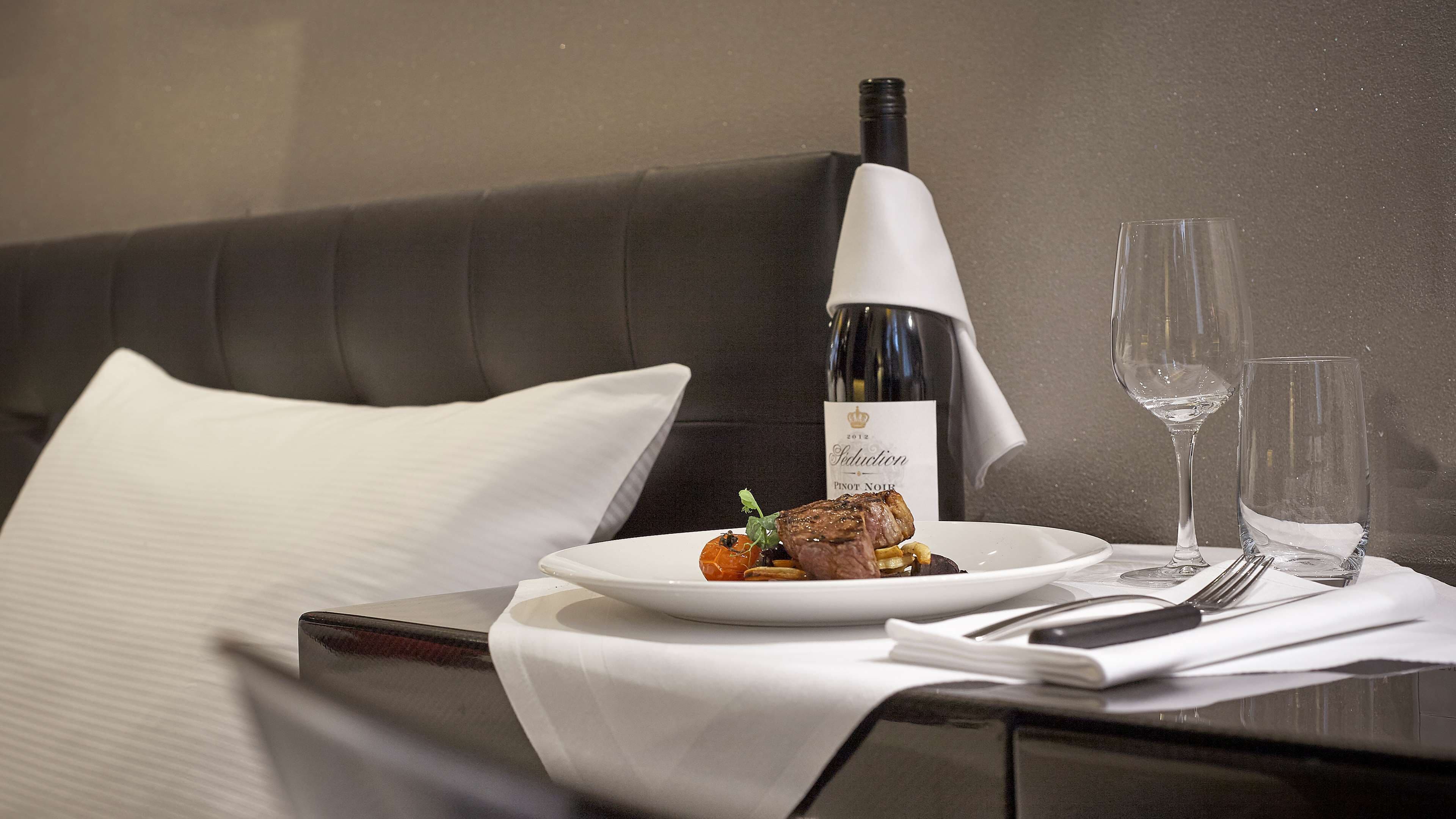 A neatly arranged dining table with a plate of food, a bottle of wine, and two glasses.