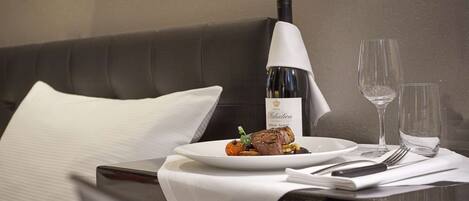 A neatly arranged dining table with a plate of food, a bottle of wine, and two glasses.
