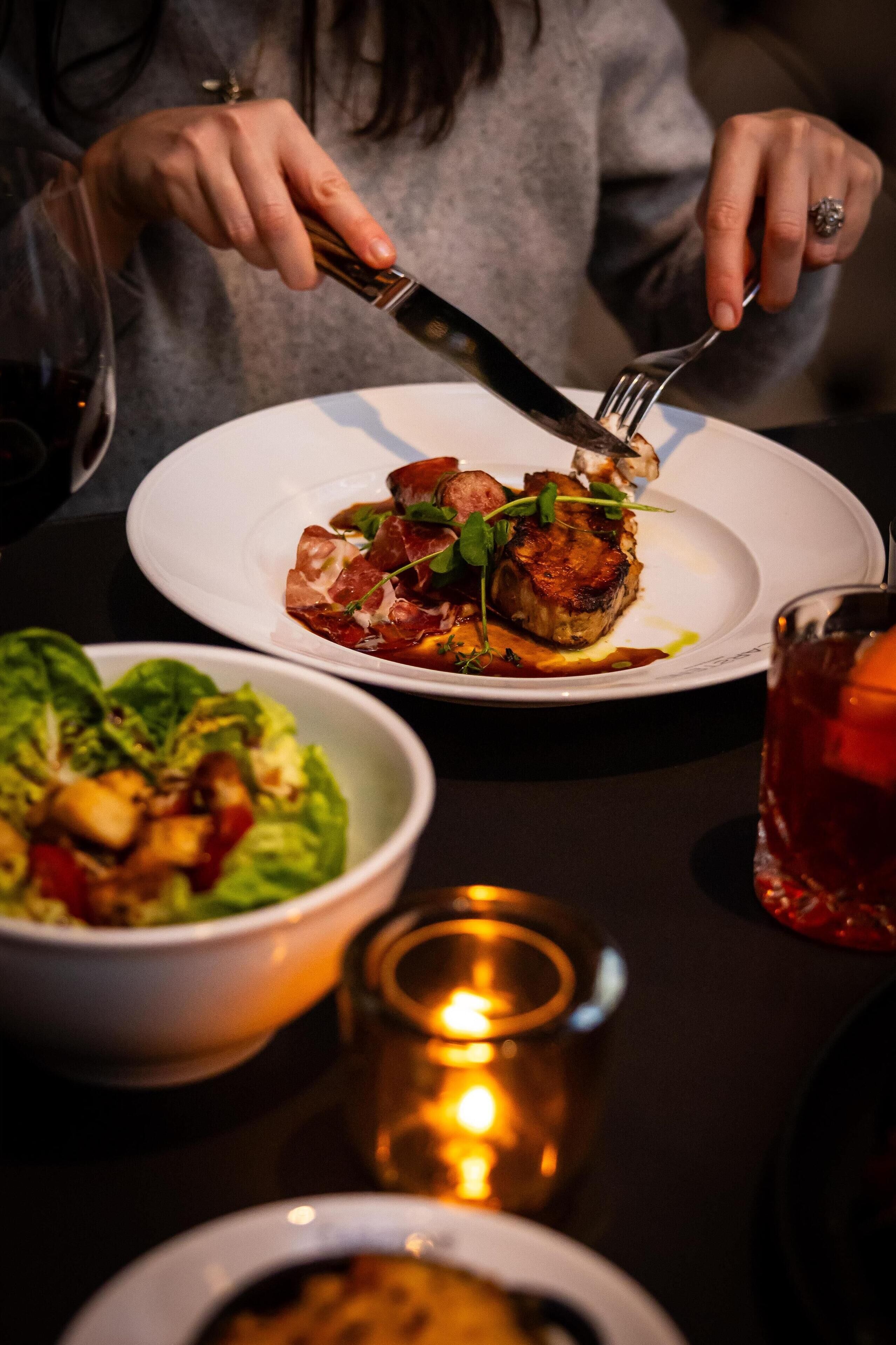 A person dining with a plate of food, a candle, and a glass of drink on the table.