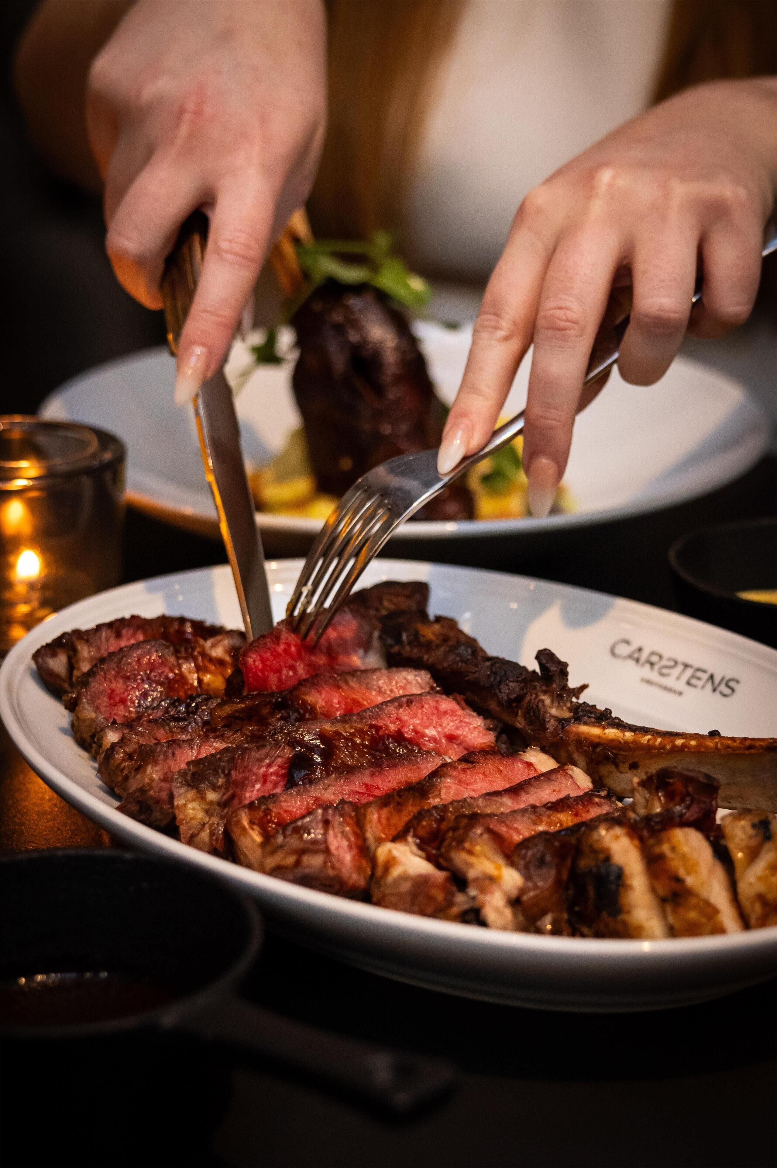 Iemand snijdt een steak op een bord met een vork en mes.