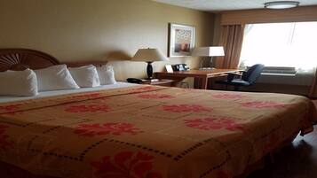 A hotel room with a large bed, a desk with a chair, a lamp, and a window with curtains.