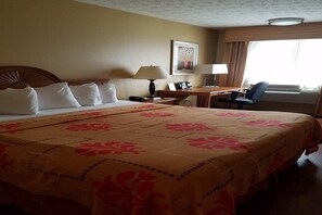 A hotel room with a large bed, a desk with a chair, a lamp, and a window with curtains. - Kennesaw Inn (Kennesaw)