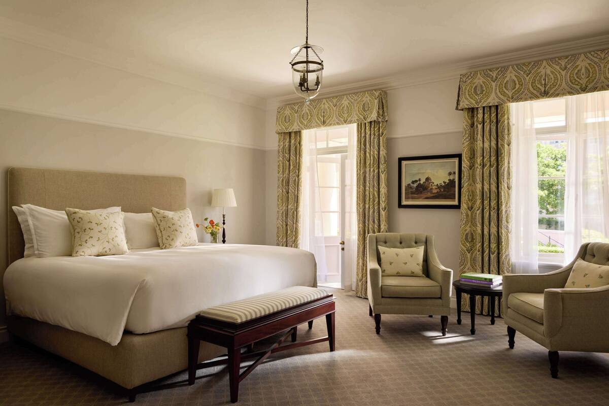 Habitación de hotel con una cama grande, dos sillones, un banco, una mesita y una araña.