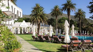 A poolside area with lounge chairs and umbrellas, palm trees, and a building with a sign reading "Librista Spa". - Mount Nelson, A Belmond Hotel, Cape Town (Cape Town)