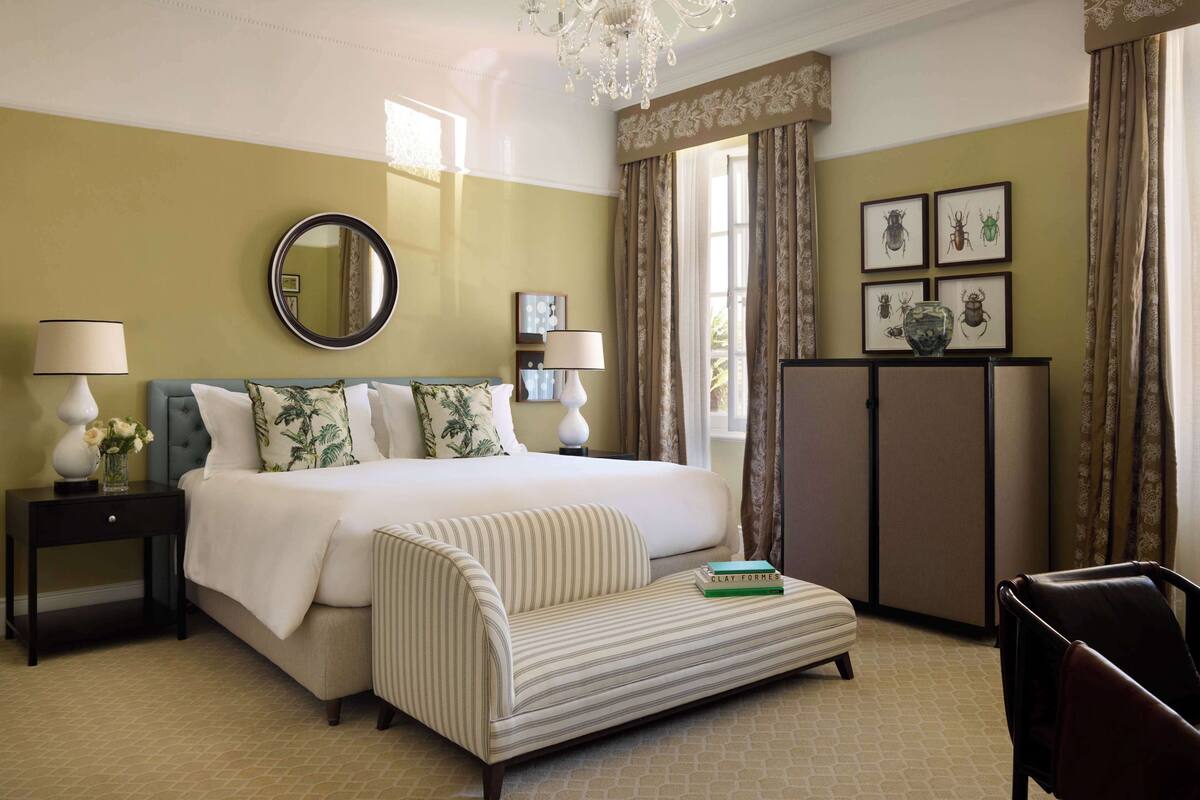 Una habitación de hotel con una cama, una mesita de noche con lámparas, un sofá, una silla, un escritorio y una araña.