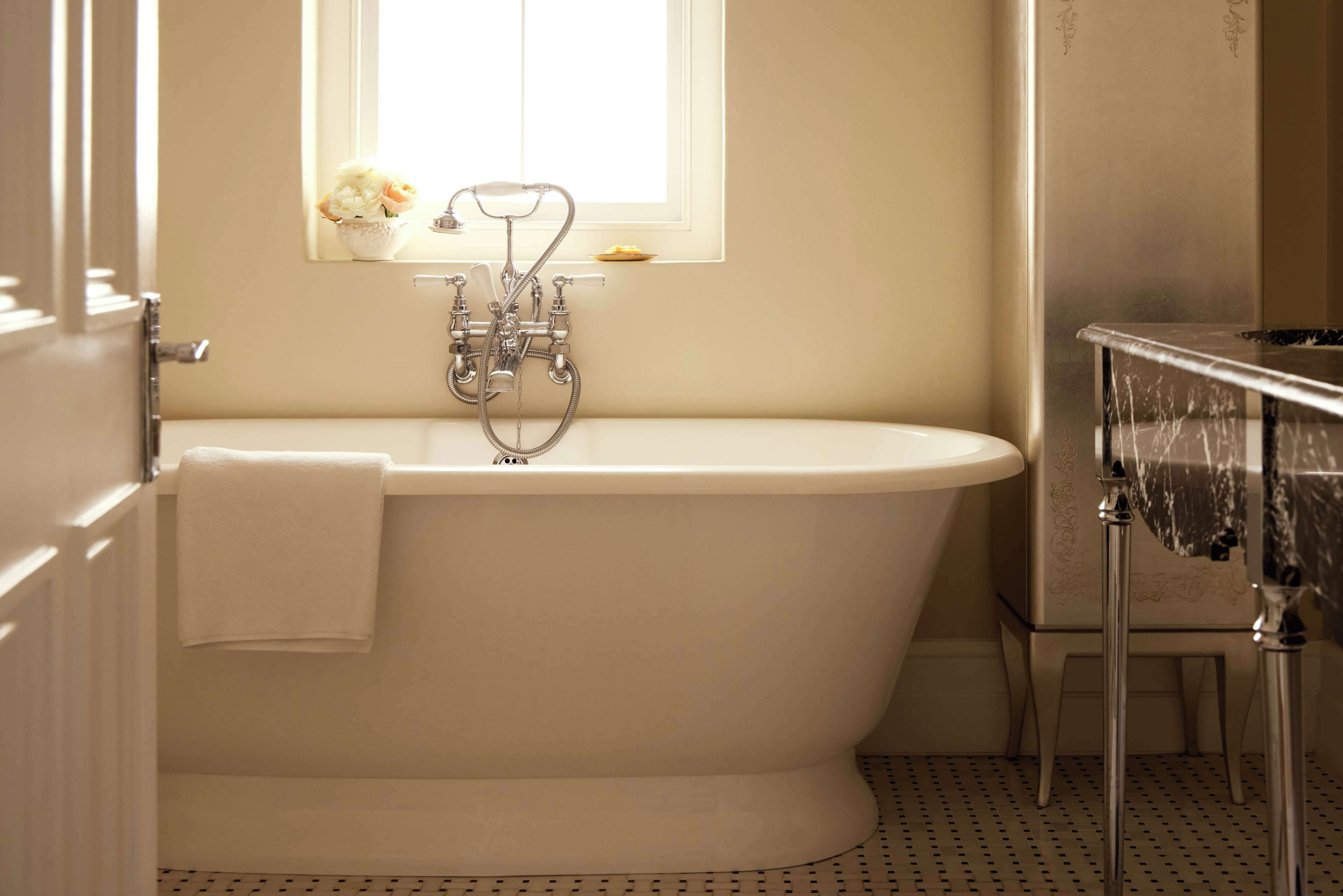 A bathroom with a freestanding bathtub, a window with a flower vase, and a tiled floor.