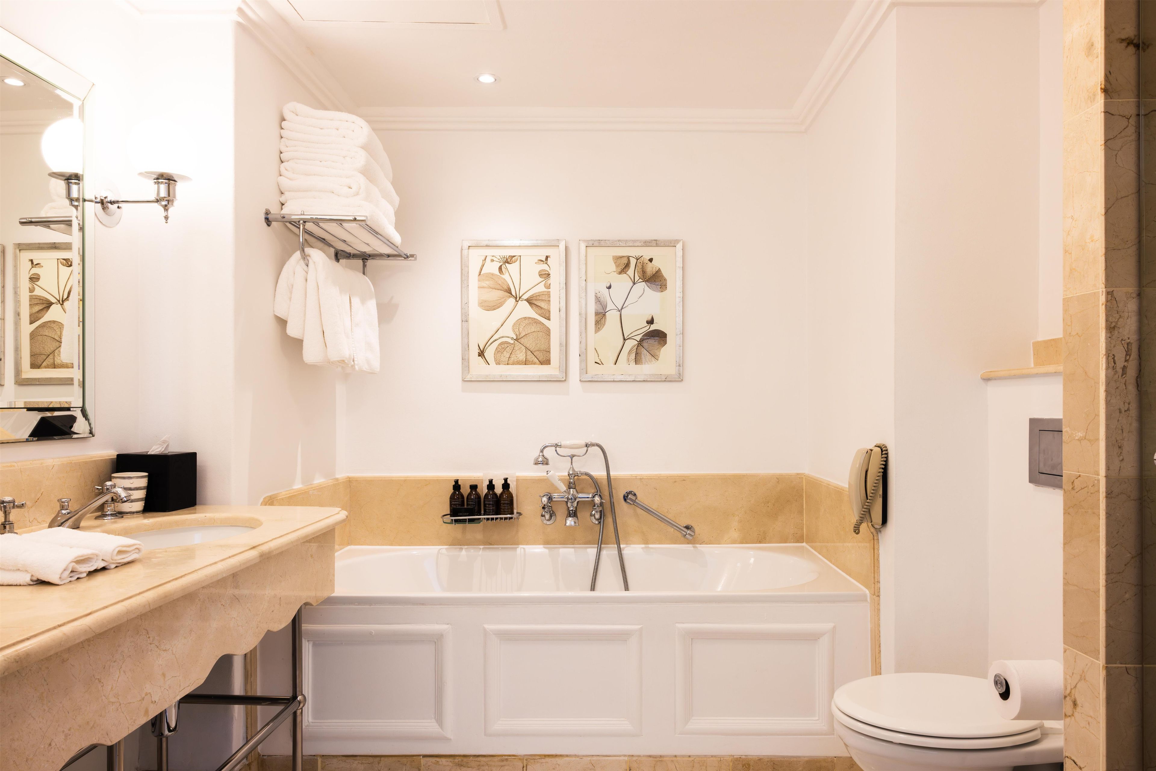 A bathroom with a bathtub, a toilet, and a sink. There are towels on the wall and a framed botanical print.