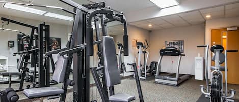 Un gimnasio con diferentes máquinas de ejercicio, una cinta de correr y un espejo grande.