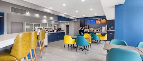 A modern restaurant with a bar area, yellow and blue chairs, and a light wood floor.