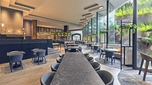 A modern restaurant with a long marble table, dark chairs, and a bar area. - Vibe Hotel Singapore Orchard (Singapore)