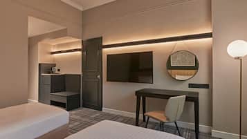 Habitación de hotel con cama, escritorio, silla, armario, espejo y lámpara de pie.