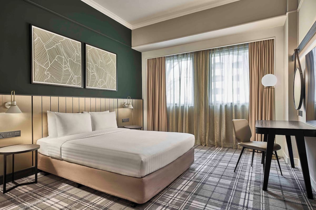 Una habitación de hotel con una cama grande, dos obras de arte colgadas en la pared, un escritorio con silla y un ventanal con cortinas.