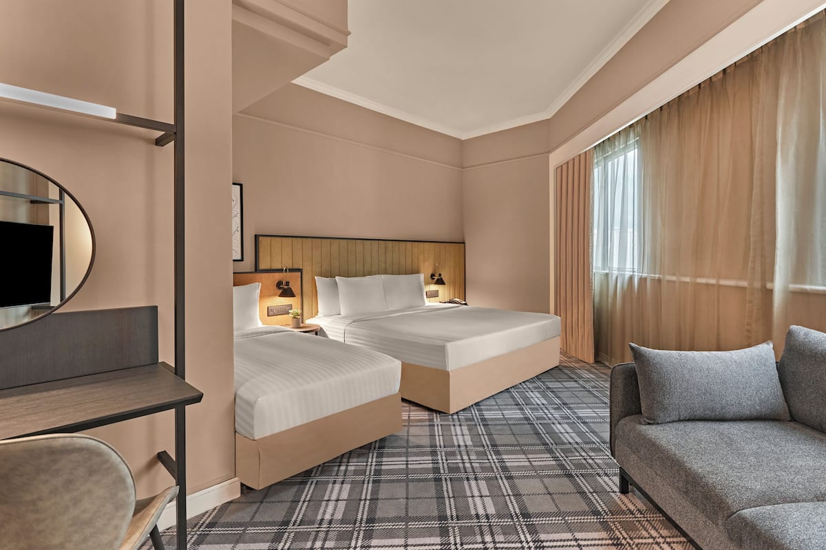 Habitación de hotel con dos camas, un sofá, un escritorio, un televisor y un ventanal con cortinas.