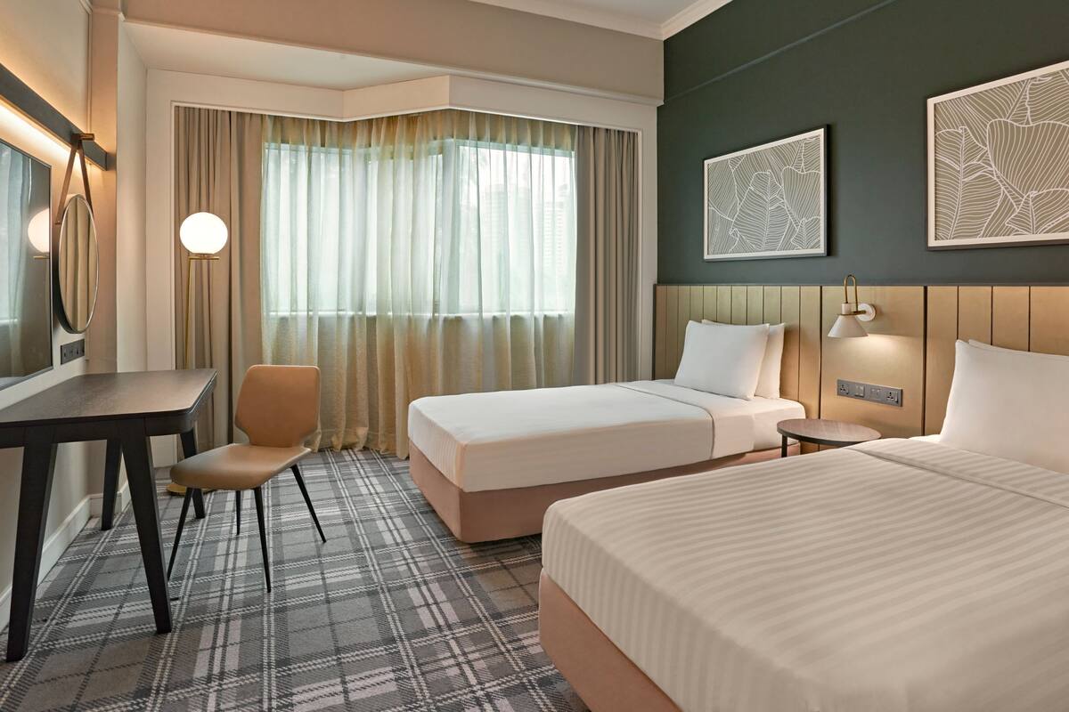 Habitación de hotel con cama, escritorio, silla, lámpara y obras de arte en las paredes.