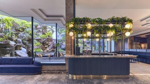 A modern lobby with a central bar area, seating arrangements, and a large window offering a view of a rocky landscape with greenery. - Vibe Hotel Singapore Orchard (Singapore)