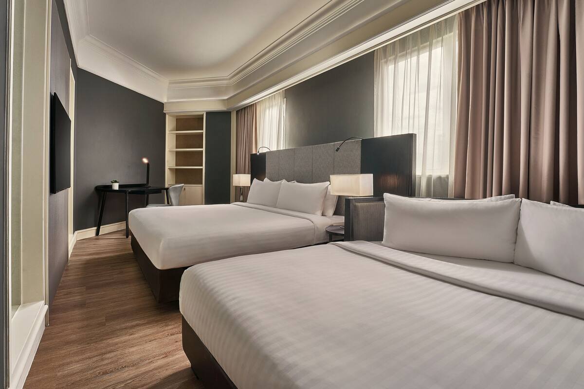 Una habitación de hotel con dos camas, un escritorio, una silla, un televisor y una lámpara.