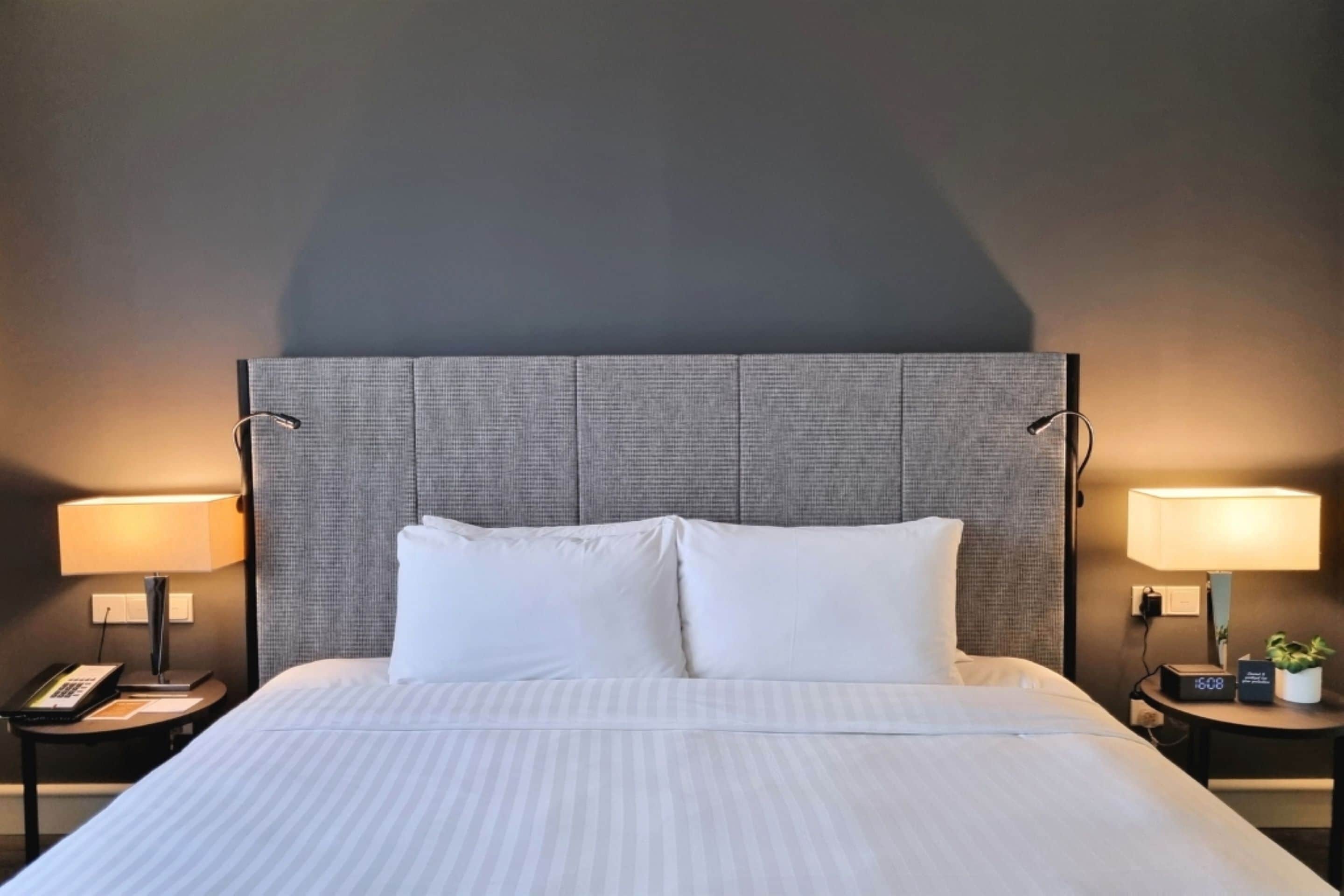 Quarto de hotel com uma cama grande, duas mesas de cabeceira e uma cabeceira moderna.