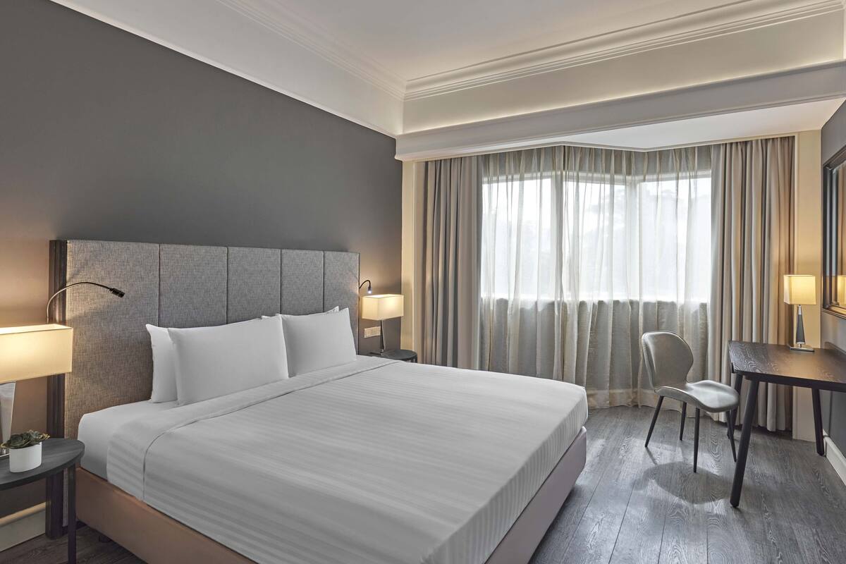 Una habitación de hotel con una cama grande, un escritorio con silla, una lámpara y una ventana con cortinas.