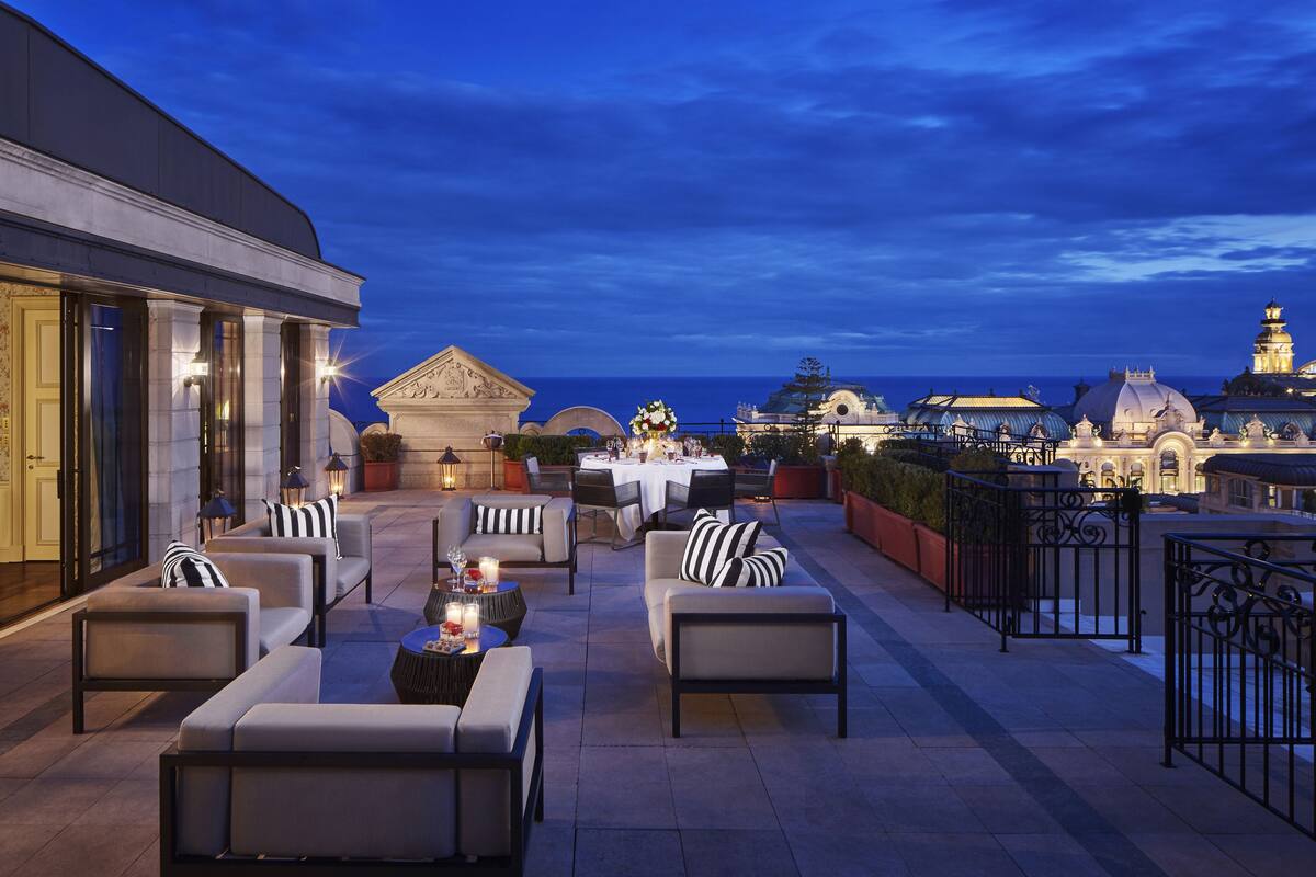 A rooftop terrace with outdoor seating, a dining area, and views of a historic building and the sea.