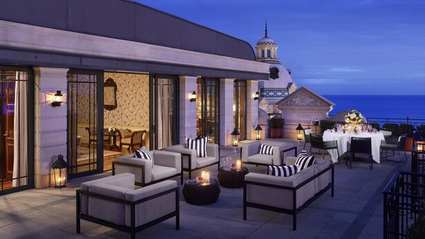 An outdoor seating area with sofas and tables, a fountain, and a view of the sea. - Hôtel Métropole Monte Carlo – Spa Guerlain (Monaco)