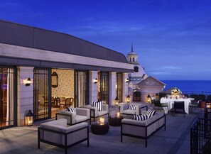 An outdoor seating area with sofas and tables, a fountain, and a view of the sea. - Hôtel Métropole Monte Carlo – Spa Guerlain (Monaco)