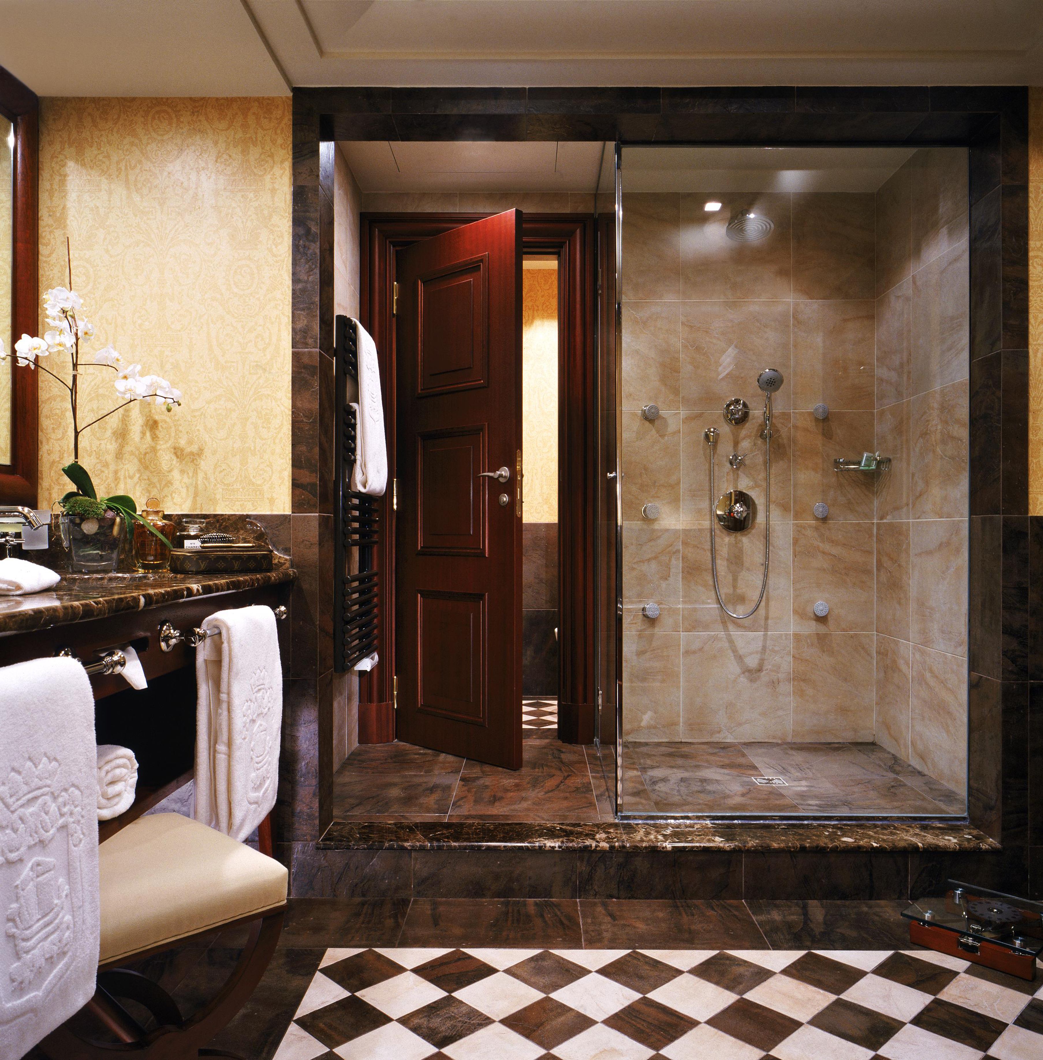 Un baño con piso de mármol, ducha con mampara de vidrio, tocador con espejo y una orquídea en maceta.