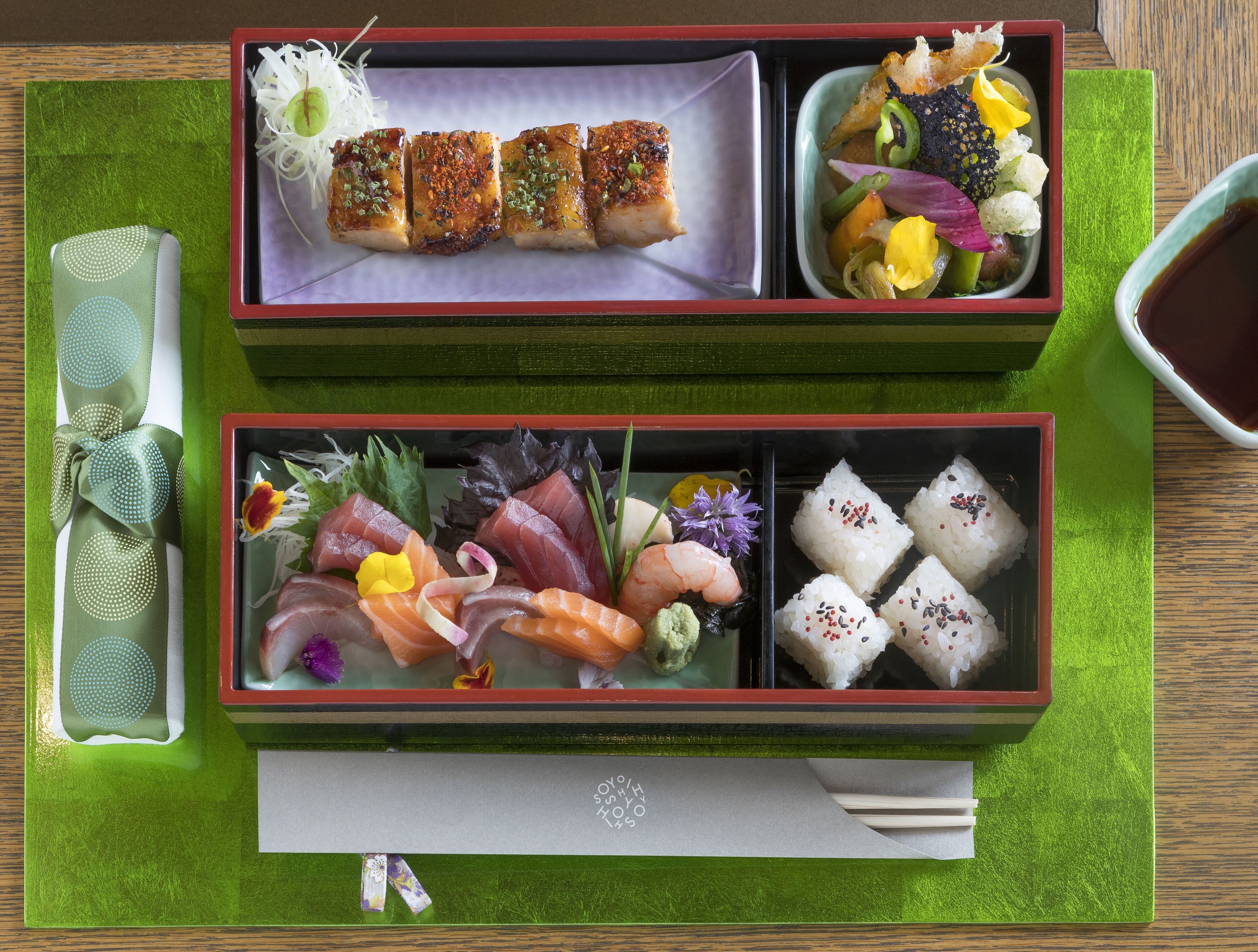 Una tradizionale bento giapponese con diversi tipi di sushi e piatti a base di riso, accompagnata da un tovagliolo verde e una piccola ciotola di salsa di soia.