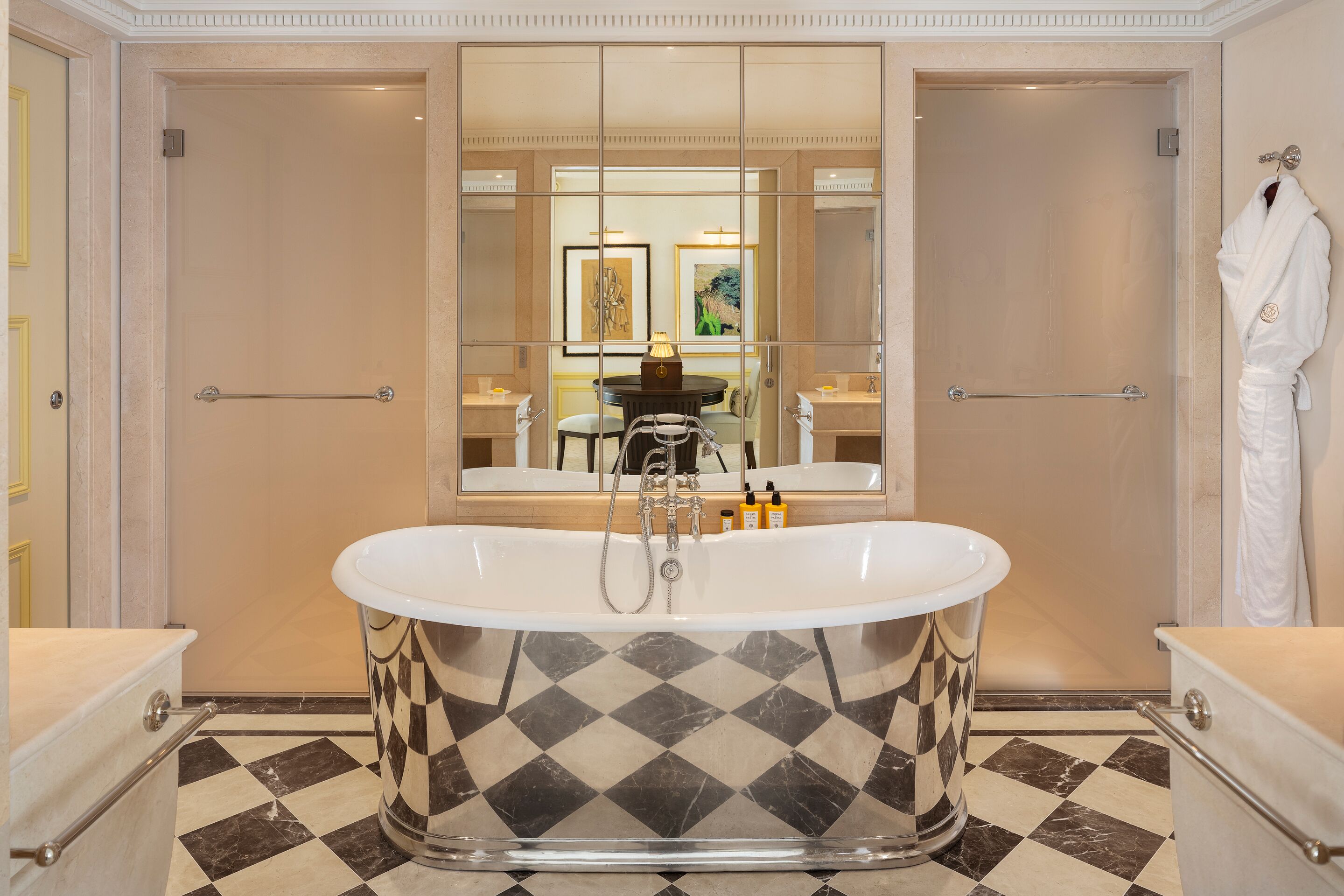 Une salle de bain avec une baignoire sur pieds, un grand miroir et un carrelage à motifs carrés.