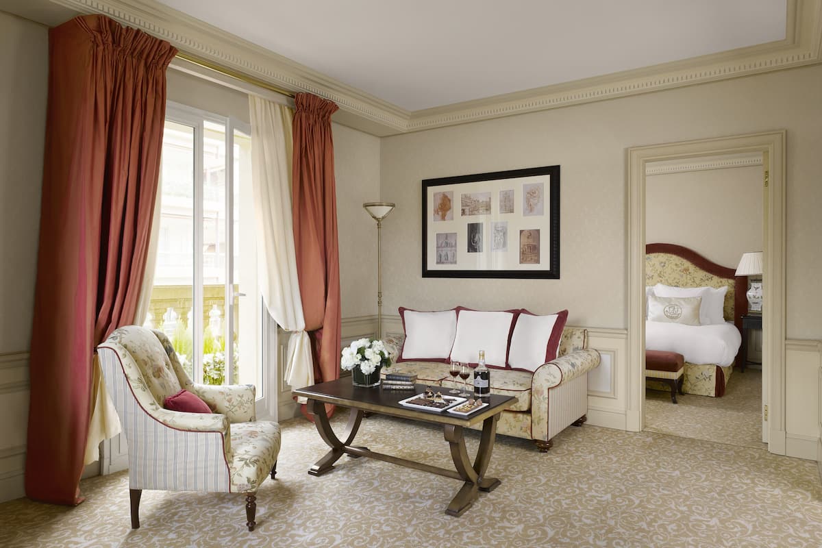 A room with a sofa, armchair, and a table with a vase of flowers and a bottle.
