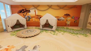 Ein Zimmer mit zwei Zelten, einem Wandgemälde einer afrikanischen Savanne und einem runden Tisch mit einer Spitzentischdecke.