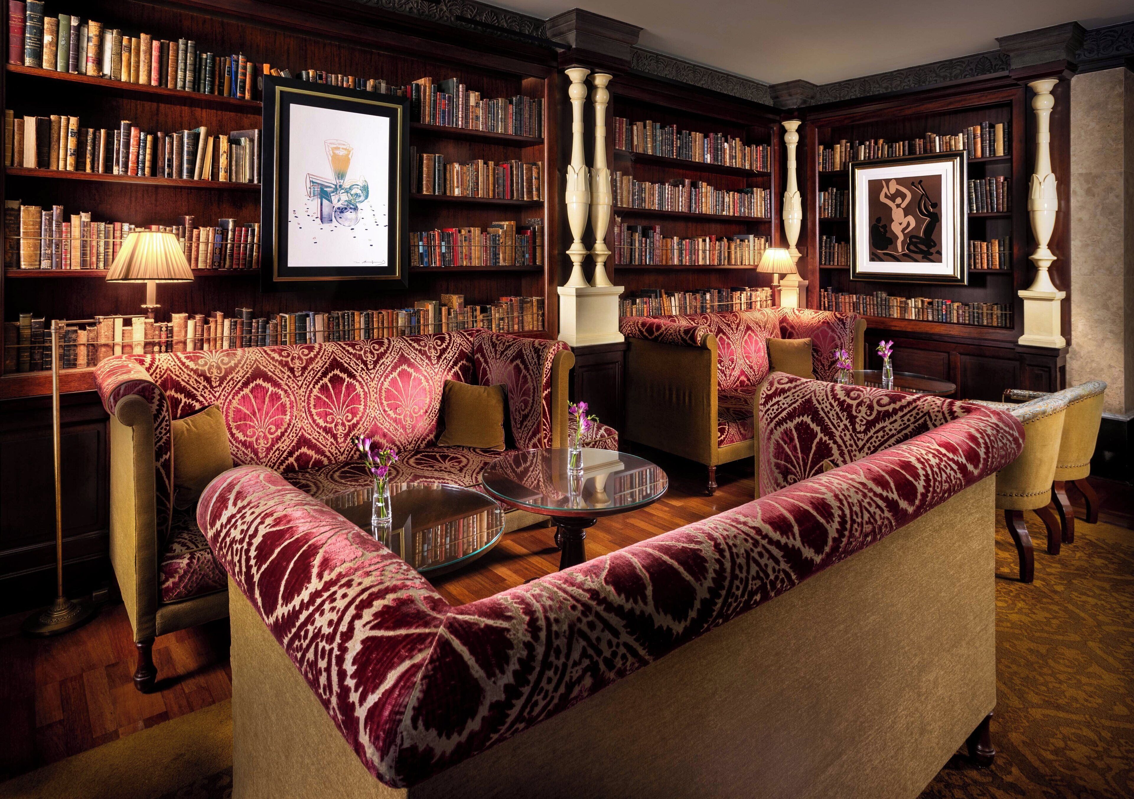 Una biblioteca con un sofá estampado, estanterías y obras de arte enmarcadas.