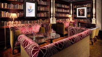 Una biblioteca con un sofá estampado, estanterías y obras de arte enmarcadas.