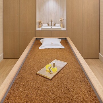 A room with a bed, a mirror, and a small table with a bottle and a candle.