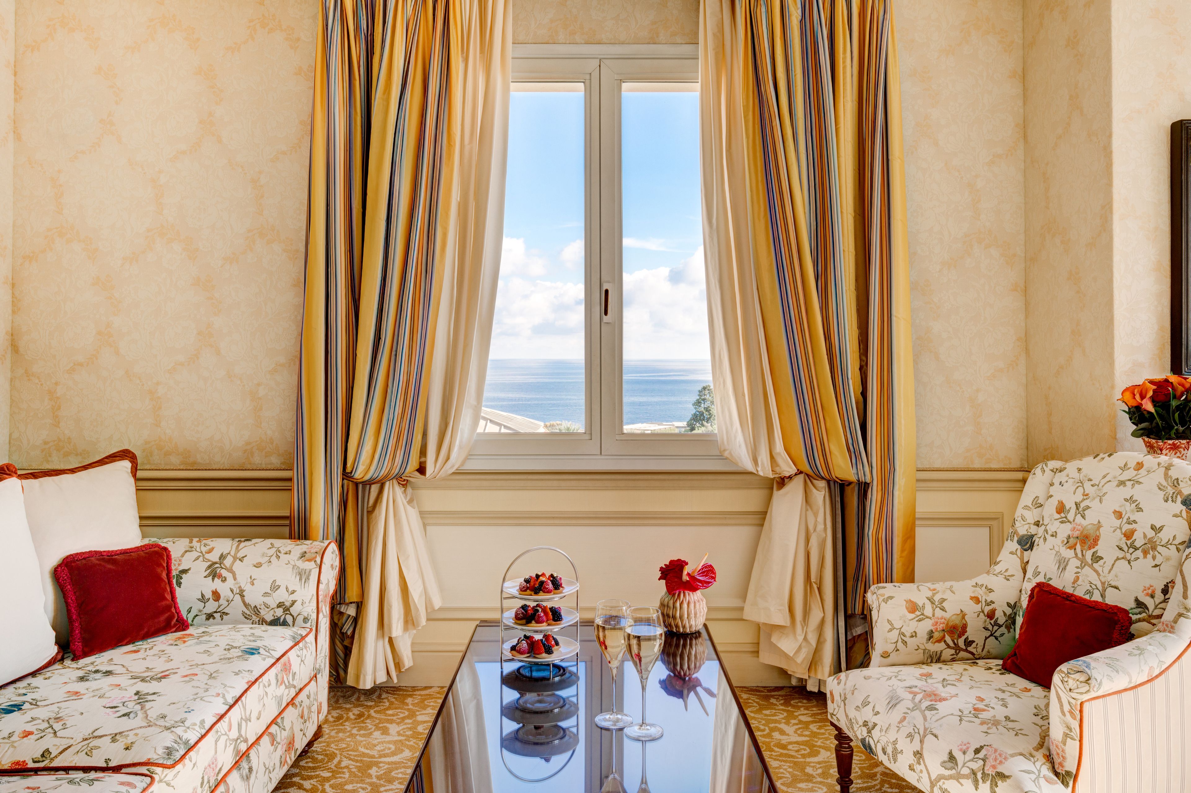 A room with a sofa, armchair, and a table with a dessert display and glasses.