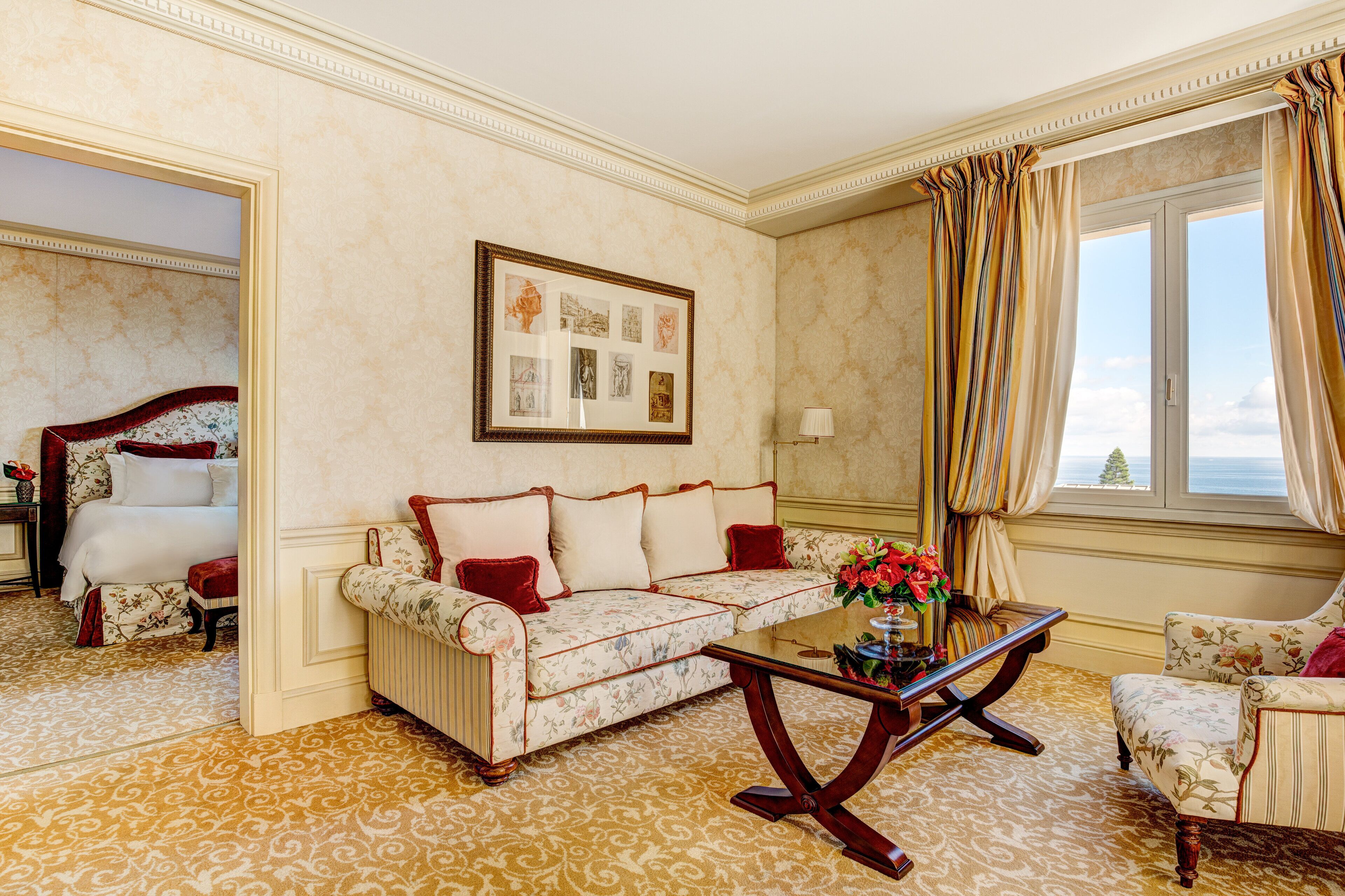 A hotel room with a floral patterned carpet, a sofa set, a coffee table, and a framed artwork on the wall.