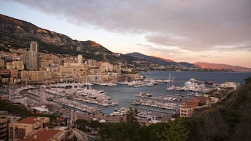 A marina with numerous boats docked, surrounded by a cityscape with buildings and mountains in the background.