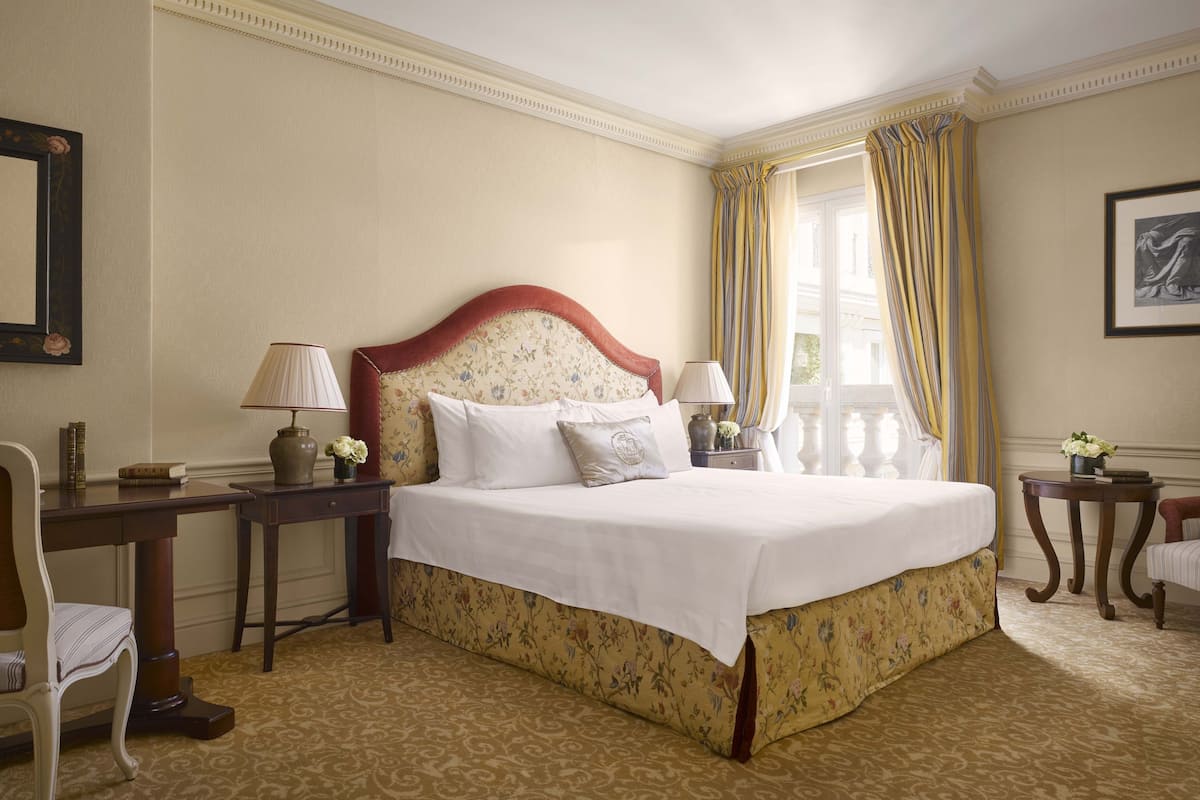 A hotel room with a large bed, two bedside tables, a chair, and a window with curtains.