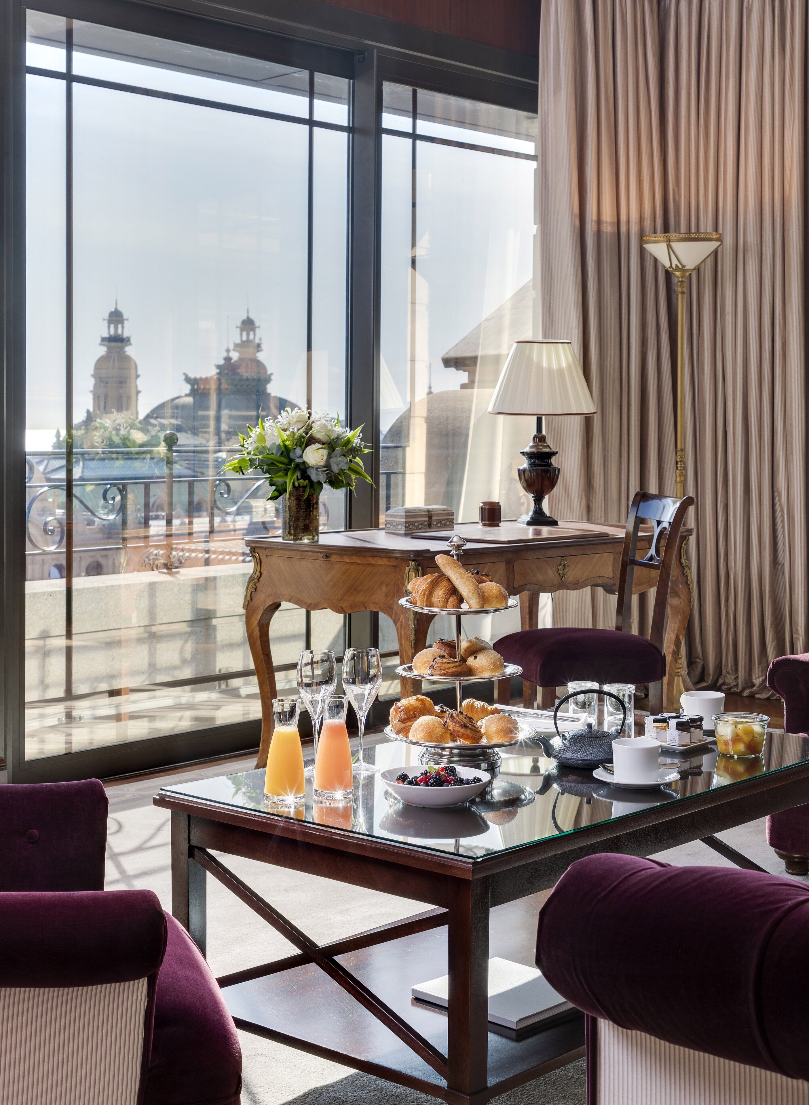 A breakfast setup with pastries, drinks, and a view of a cityscape through large windows.