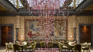 A grand lobby with a large mural, elegant green chairs, and a chandelier. - Hôtel Métropole Monte Carlo – Spa Guerlain (Monaco)
