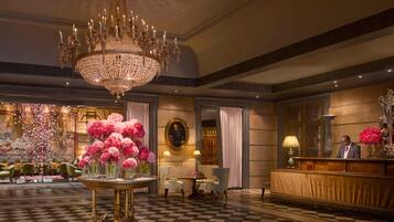 Un'ampia hall con un grande lampadario, pavimento a scacchi e una reception.