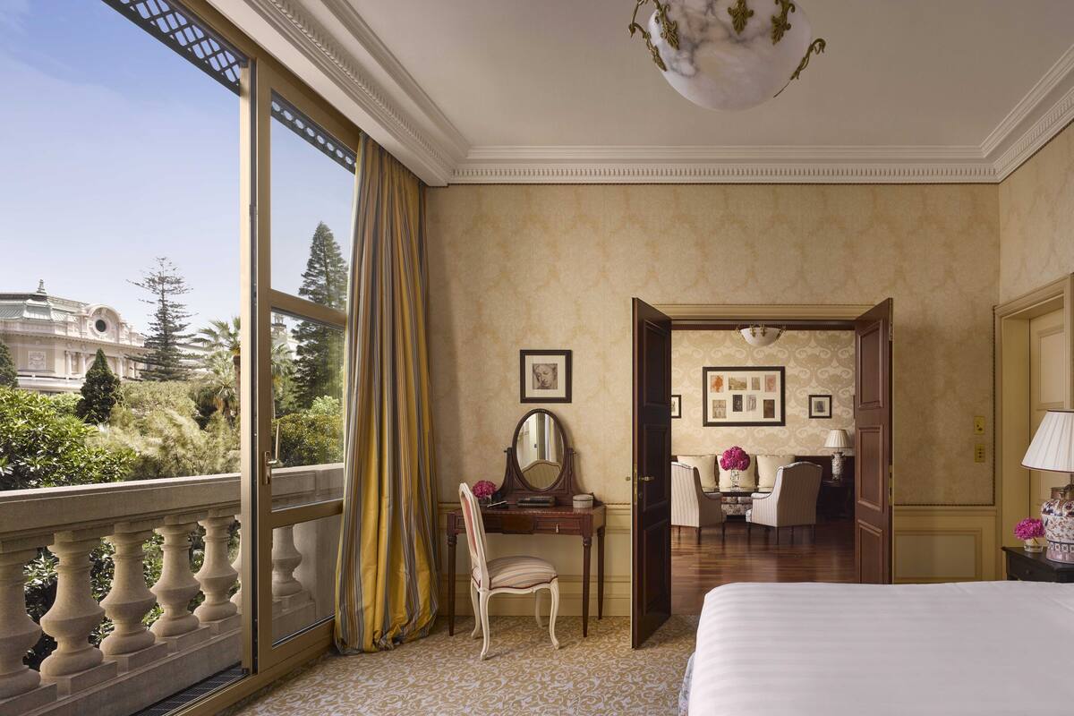 A hotel room with a large bed, a desk with a chair, a mirror, and a view of a building outside.