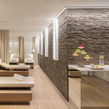 A modern spa room with massage tables, a stone wall, and a reception area with a decorative lamp.