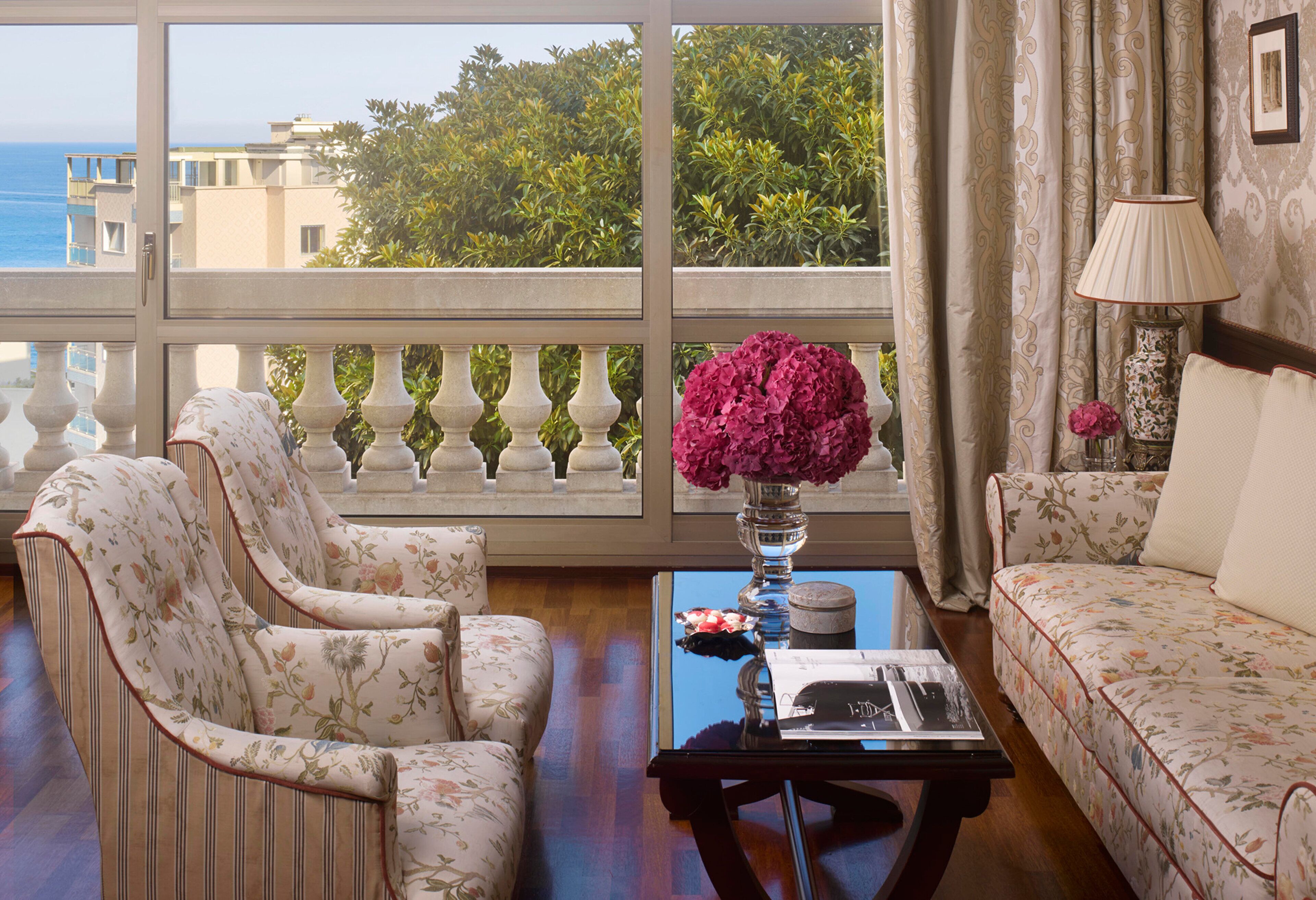 Un salon avec vue sur la mer, un canapé, un fauteuil, une table avec un vase de fleurs et une lampe.