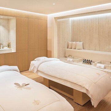 A modern spa room with two treatment beds, a large mirror, and a vanity with a sink and shelves.