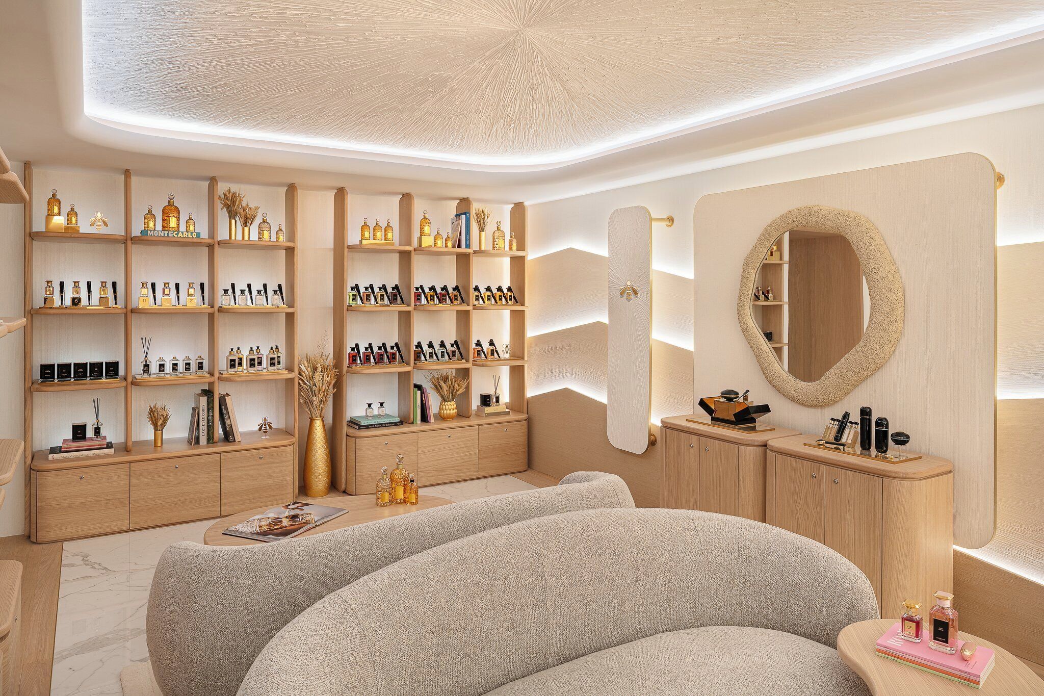 A modern, well-lit room with wooden shelving displaying various bottles and books, a large mirror, and a comfortable seating area.