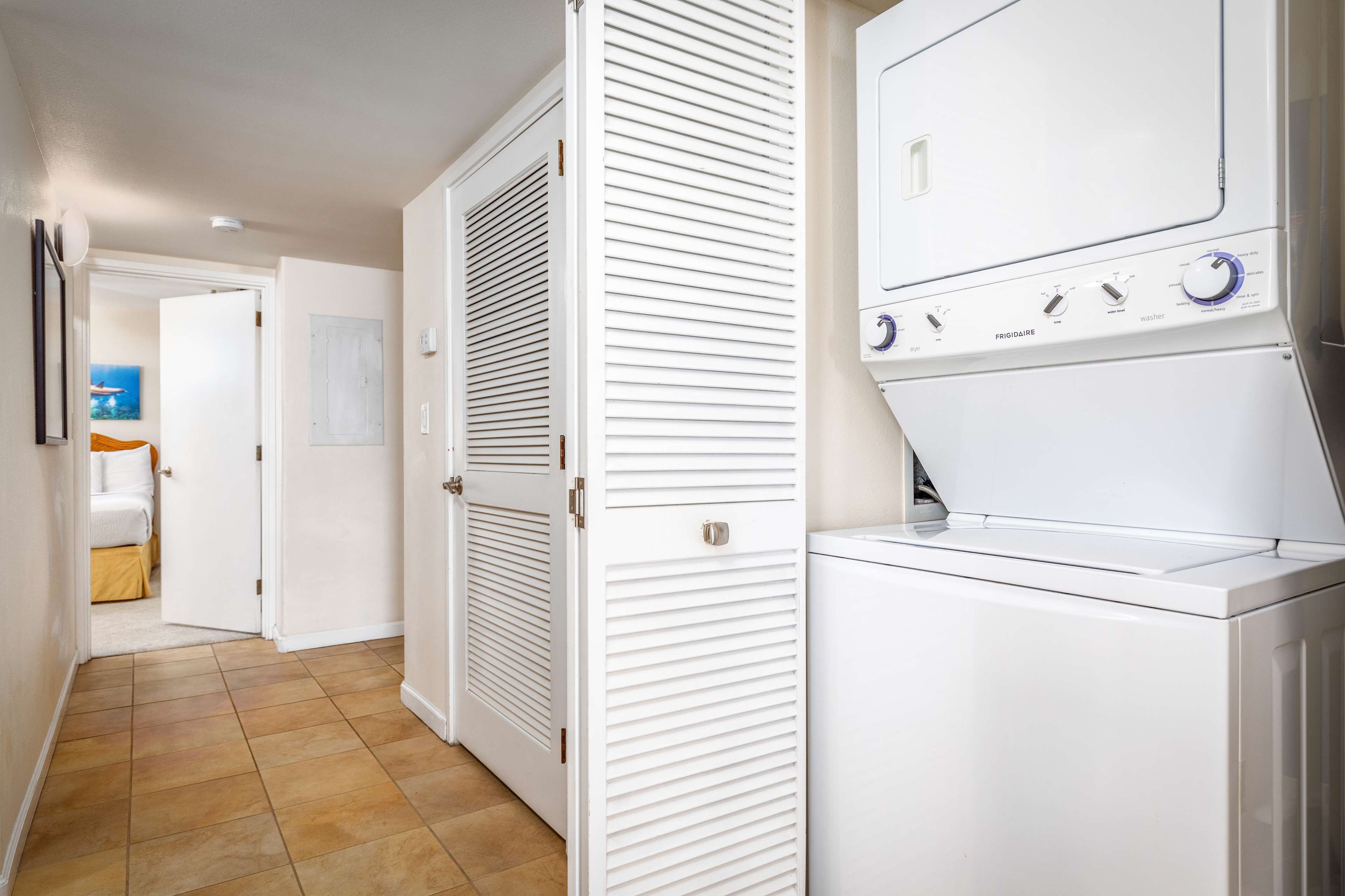 Une buanderie équipée d’un lave-linge et d’un sèche-linge à chargement frontal, de portes blanches à lattes horizontales et d’un sol carrelé.